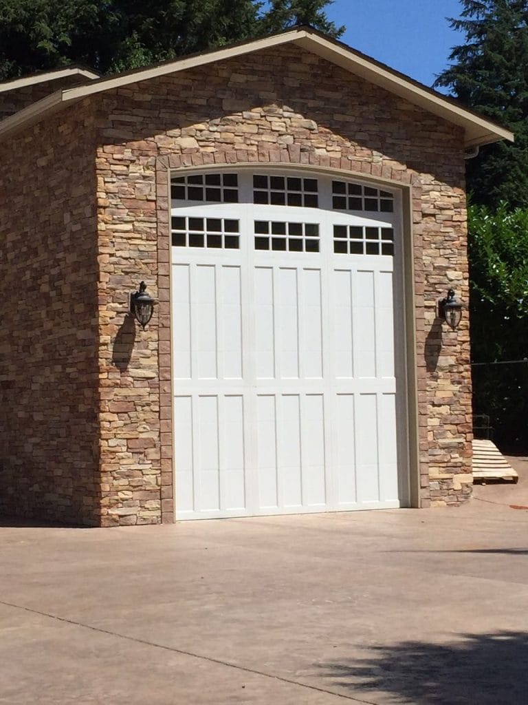White garage door with window panes between stone columns